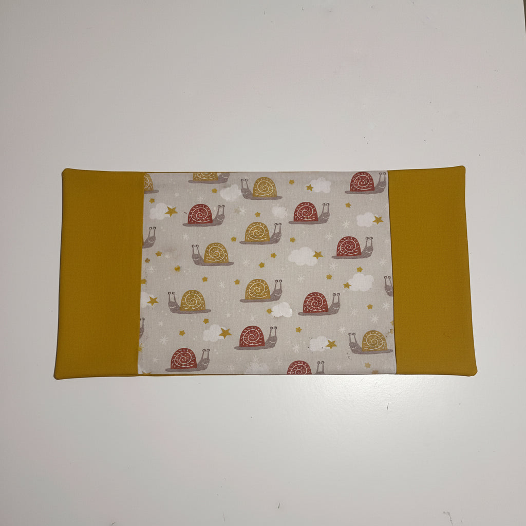 Vue dépliée du protège carnet de santé montrant le tissu central à motifs escargots rigolos et les grands rabats latéraux couleur moutarde.