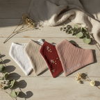 Lot de quatre bandanas bébé en coton, couleurs naturelles et motif floral, personnalisable, posé sur bois clair.
