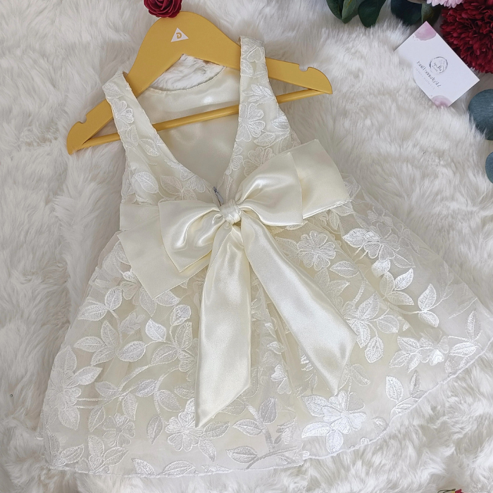Vue de dos de la robe de cérémonie blanche pour bébé présentée sur un cintre. Détail du grand nœud en satin et des broderies florales. Création artisanale.