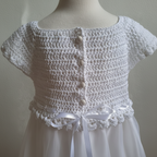 Gros plan sur le haut en crochet blanc, les boutons et le ruban en satin de la robe de baptême fille.