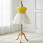 Robe d'été pour bébé fille présentée sur mannequin. Haut en crochet jaune soleil et jupe en tulle blanc parsemée de petites broderies colorées.