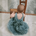 Bébé portant la robe de cérémonie vert sauge, vu de dos. Gros plan sur le grand nœud en satin et le tissu à sequins scintillants.