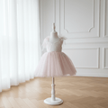 Robe de cérémonie pour enfant en tulle rose poudré pailleté avec nœuds sur les épaules, présentée de face sur un mannequin blanc.