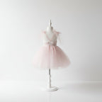 Vue de dos d'une robe de cérémonie fille en tulle rose poudré avec décolleté en V et noeuds en tulle aux épaules, sur mannequin blanc fond épuré