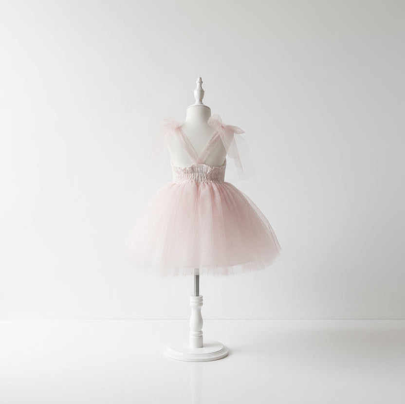 Vue de dos d'une robe de cérémonie fille en tulle rose poudré avec décolleté en V et noeuds en tulle aux épaules, sur mannequin blanc fond épuré