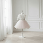 Vue de dos d'une robe de cérémonie fille en tulle rose poudré avec décolleté en V et noeuds en tulle aux épaules, sur mannequin dans un intérieur élégant