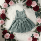 Robe de cortège bébé vert sauge mise en scène au milieu d'une couronne de fleurs. Tenue idéale pour un baptême ou un mariage champêtre.