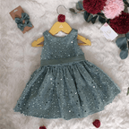Robe à paillettes vert sauge posée à plat sur fond doux, accompagnée de son duo de barrettes nœud assorties. Création artisanale Atelier de Megh.
