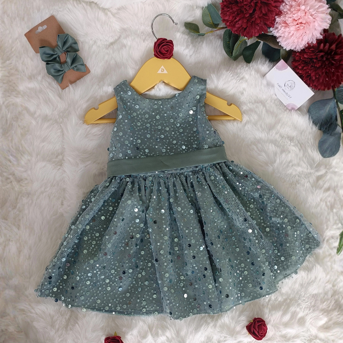 Robe à paillettes vert sauge posée à plat sur fond doux, accompagnée de son duo de barrettes nœud assorties. Création artisanale Atelier de Megh.