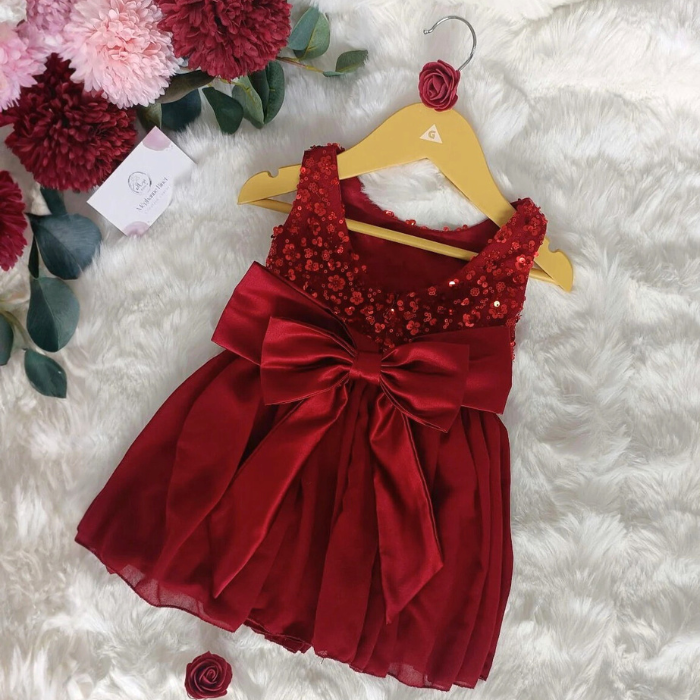 Robe de cérémonie fille rouge à paillettes présentée sur un cintre avec décoration florale. Création artisanale française Atelier de Megh.