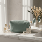 Trousse moyenne de toilette entièrement confectionnée en velours côtelé vert sauge, posée élégamment sur un meuble en marbre près d'un flacon de parfum.