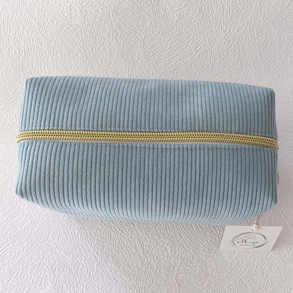 Vue de dessus d'une trousse de toilette fermée en velours côtelé doux de couleur vert sauge, montrant la fermeture éclair dorée.