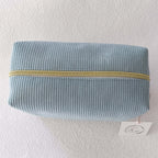 Vue de dessus d'une trousse de toilette fermée en velours côtelé doux de couleur vert sauge, montrant la fermeture éclair dorée.