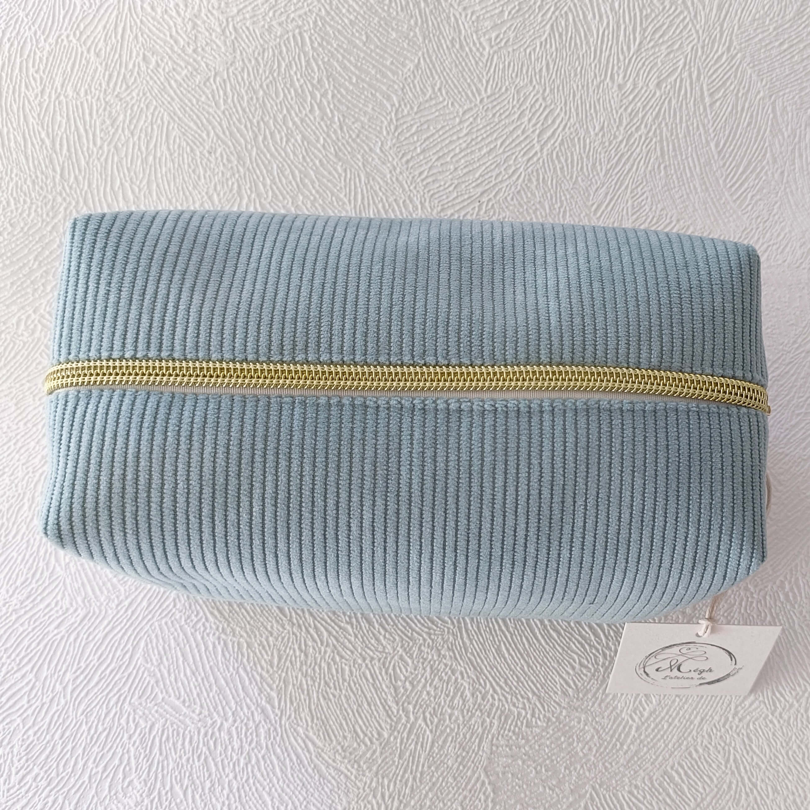Vue de dessus d'une trousse de toilette fermée en velours côtelé doux de couleur vert sauge, montrant la fermeture éclair dorée.
