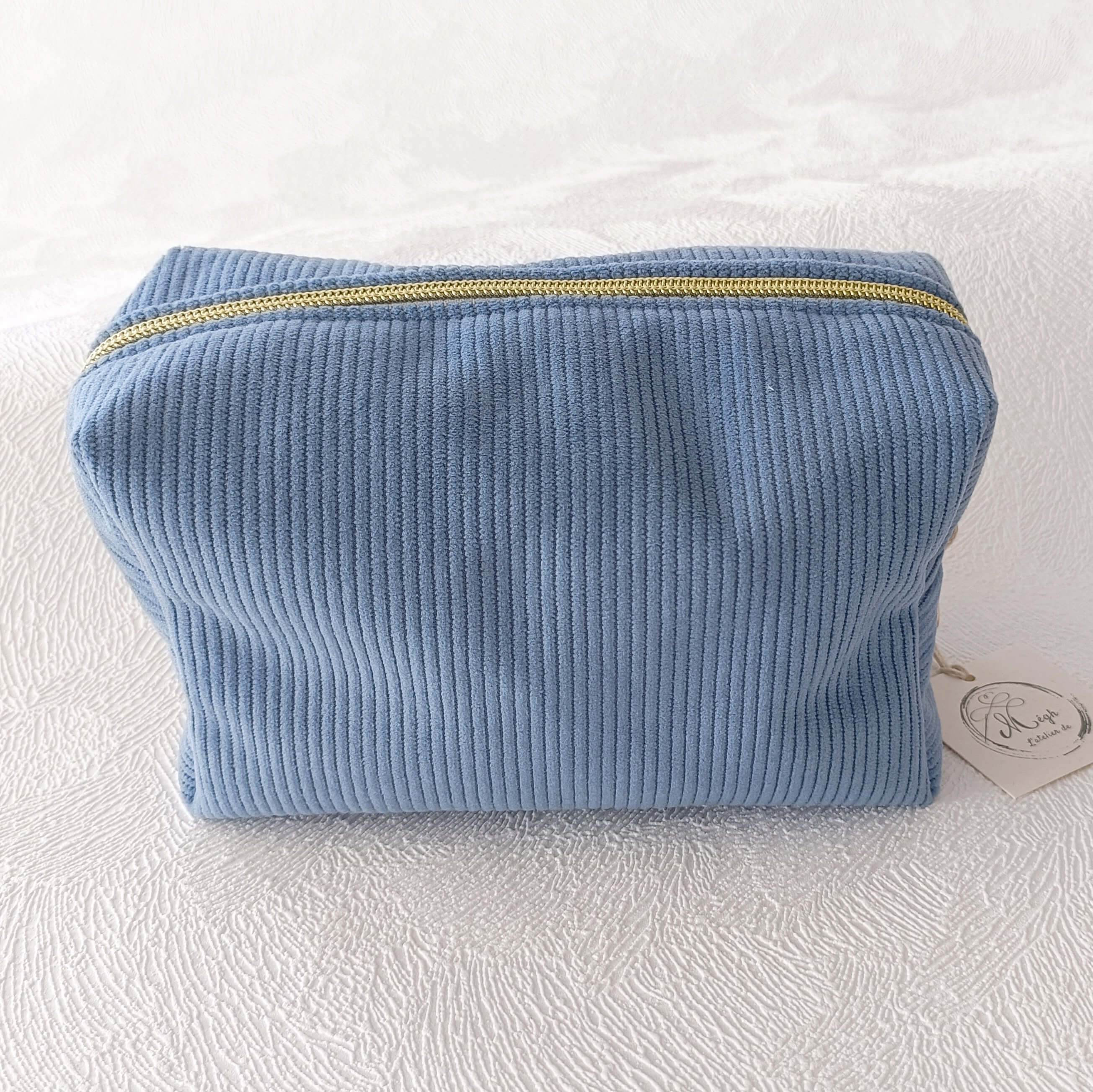 Trousse en tissu côtelé bleu avec fermeture éclair dorée, posée sur fond blanc