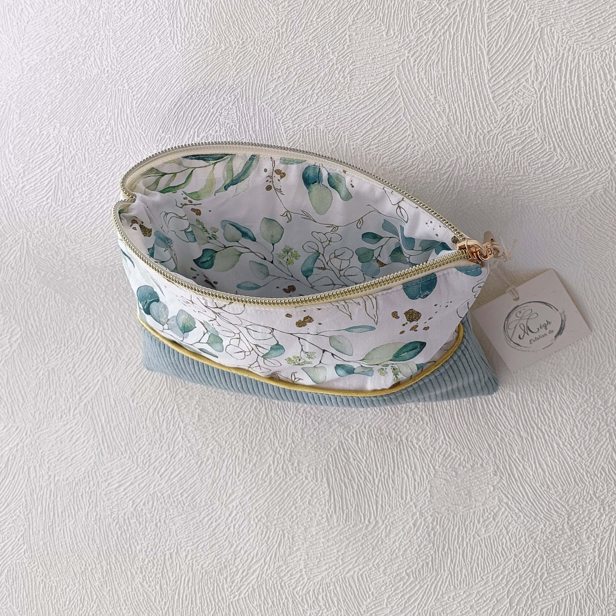 Trousse de toilette en velours vert sauge grande ouverte, permettant de voir sa capacité de rangement et sa doublure intérieure à motifs végétaux.